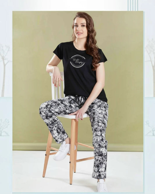 Woman seated on a stool in a black Smile Everyday tee and printed pyjama by In Touche