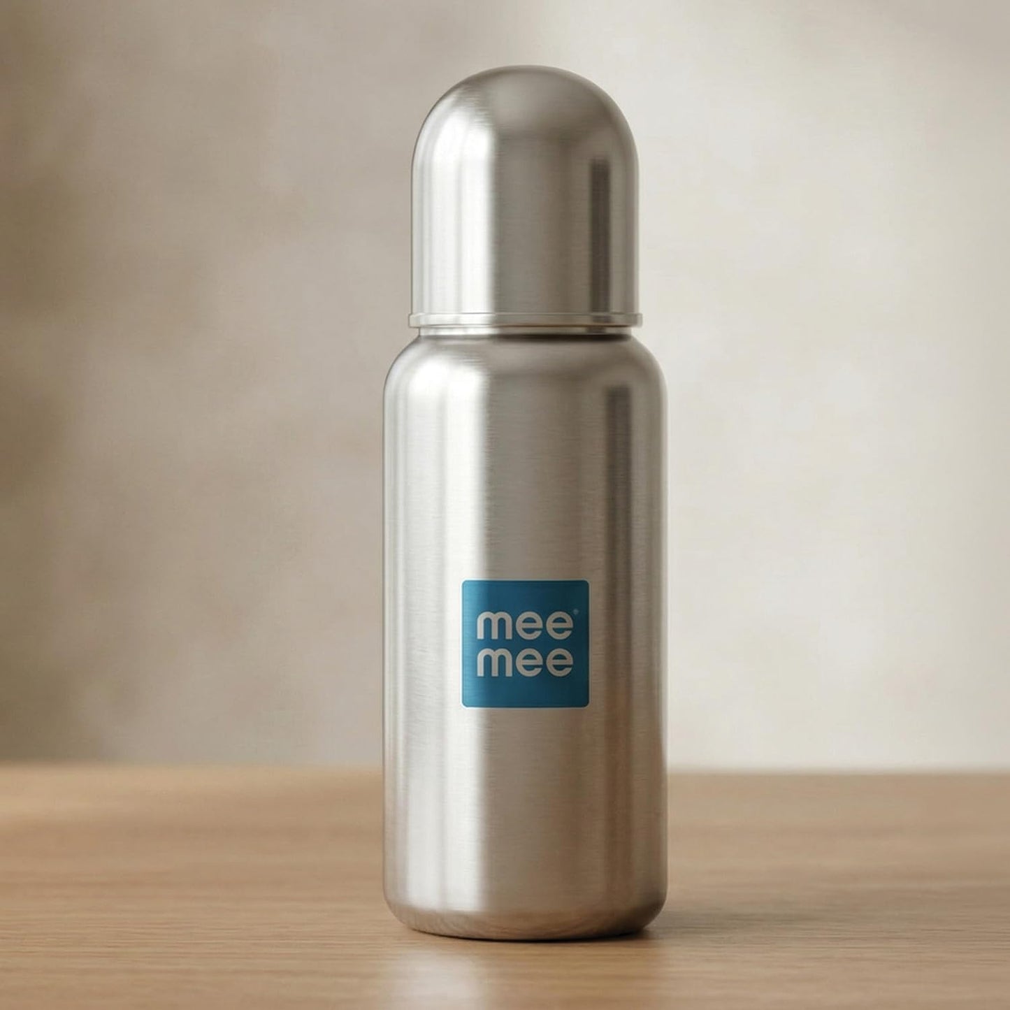 Mee Mee premium stainless steel baby feeding bottle standing on a wooden surface